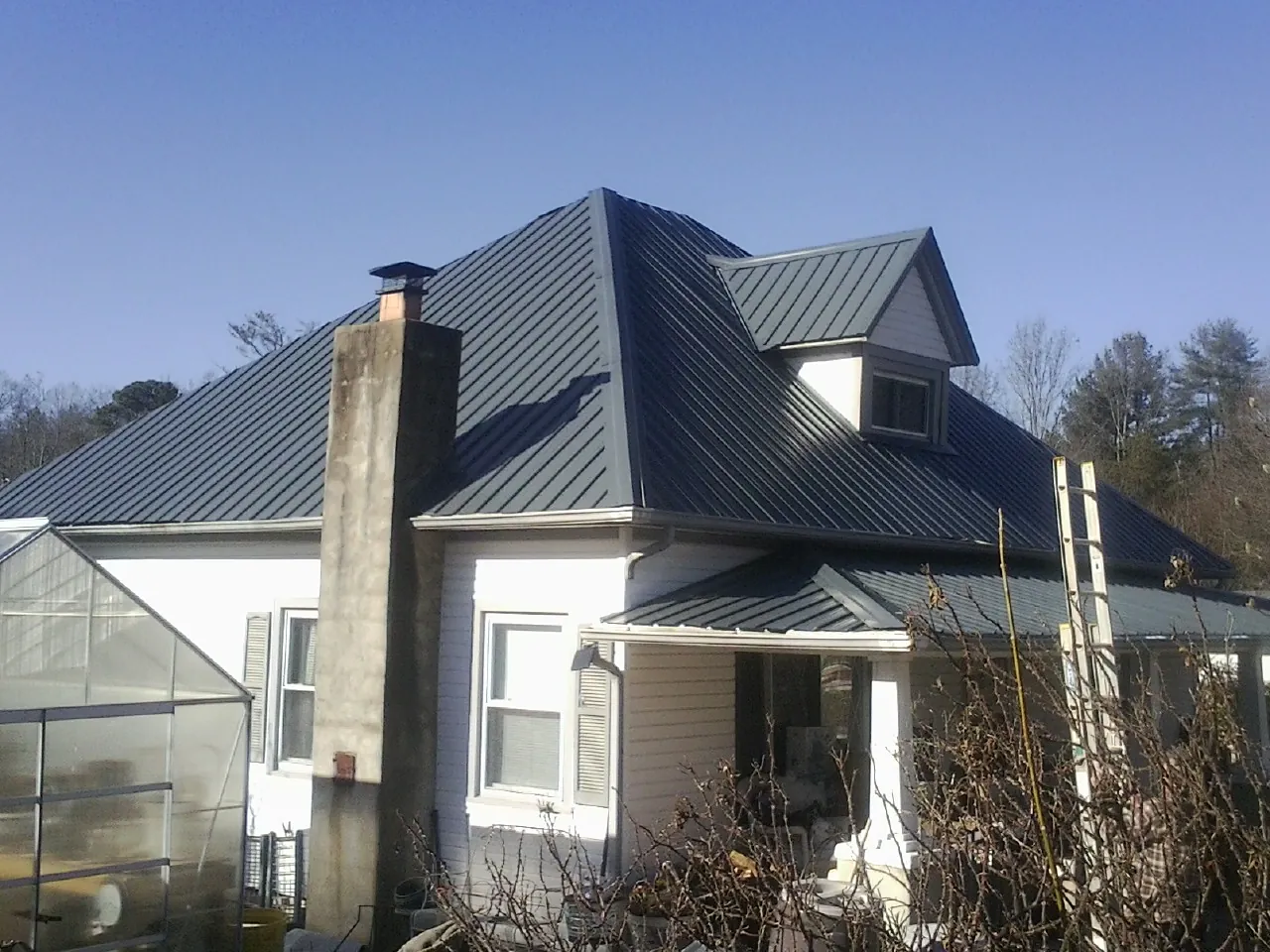 Dark blue standing seam metal roof on a white farmhouse with dormer — Slate & Tile Roof Repair by Roofing Brothers in Matamoras