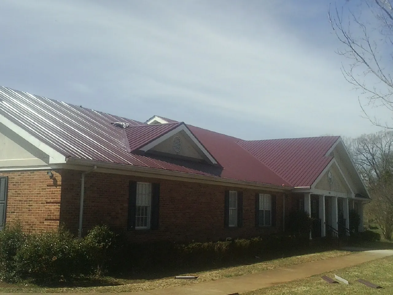 Red metal roof with gabled entries on a long brick building, from a Hail Damage Roof Repair job in Matamoras