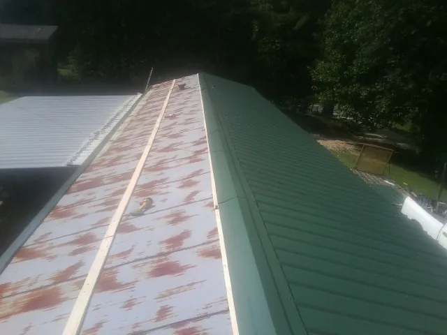 Old rusted panels beside newly installed green metal roofing — Wind Damage Roof Repair by Roofing Brothers in Matamoras