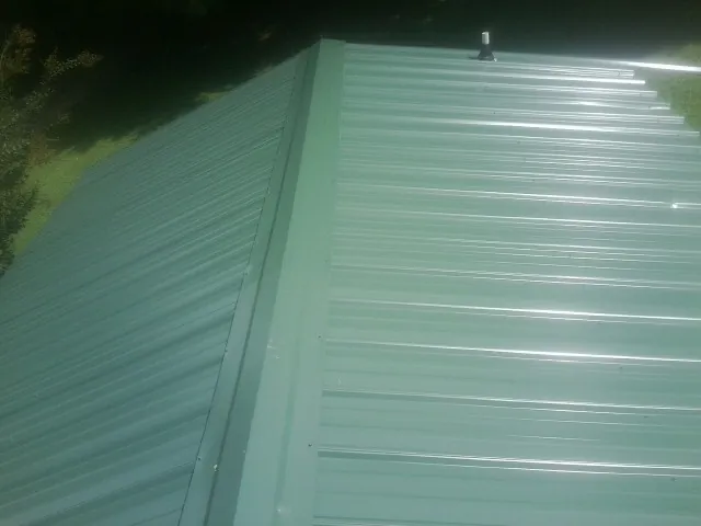 New green metal panels meeting at the ridge of a roof — Flat Roof Repair work by our crew in Matamoras