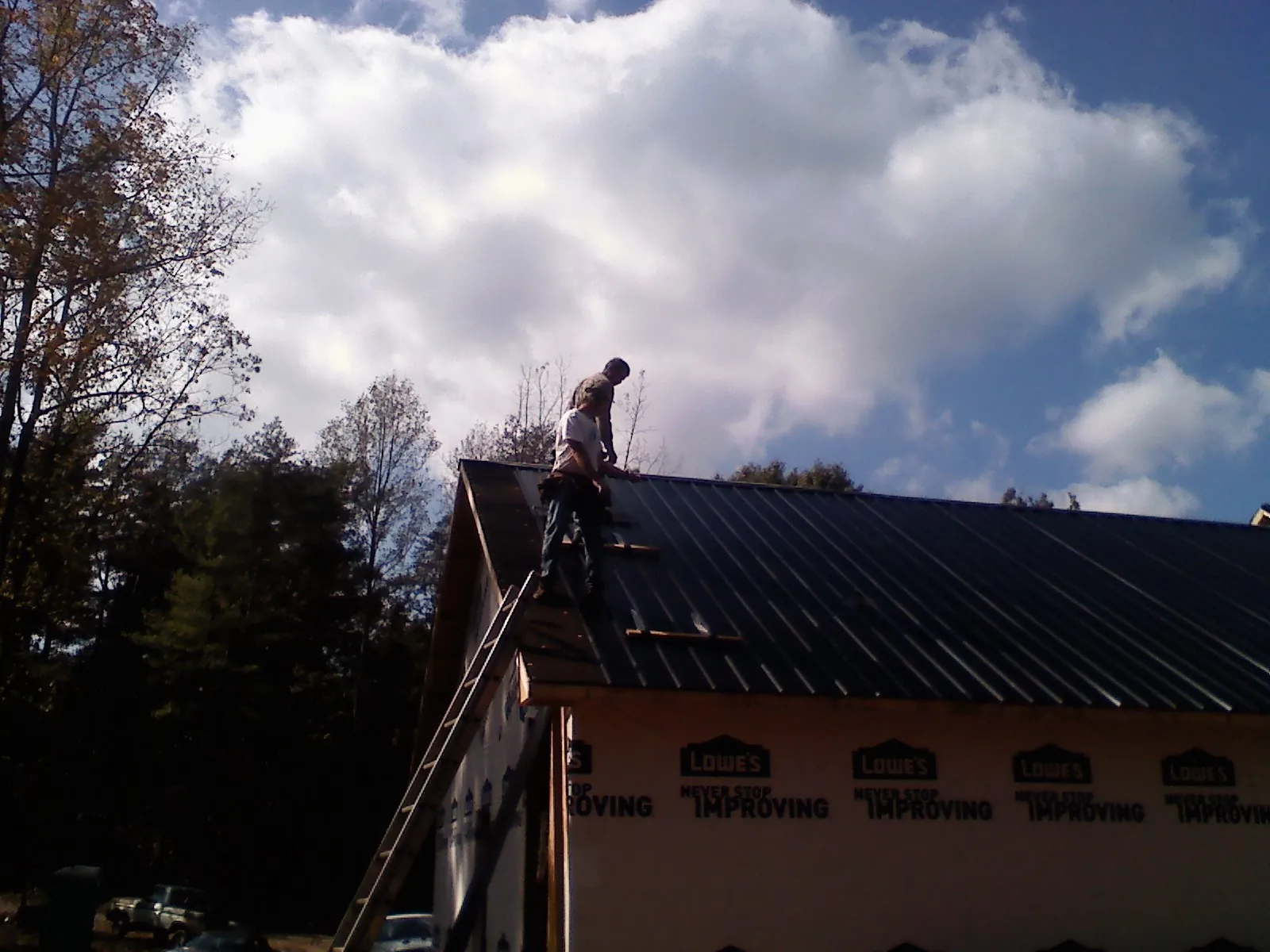 Roofer fastening dark metal panels high against a cloudy sky, from a Roof Inspection job in Matamoras