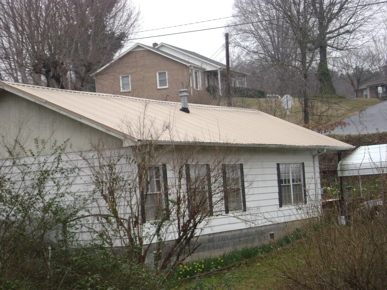 Tan metal roof on a white sided house set into a hillside — Commercial Roofing by Roofing Brothers in Matamoras