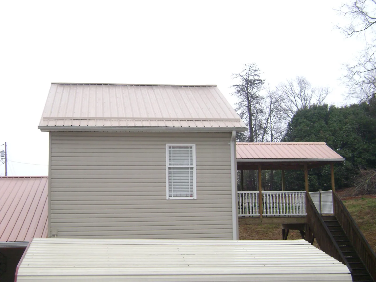 Tan metal roofs on a two story addition and attached porch, from a Roof Replacement job in Matamoras